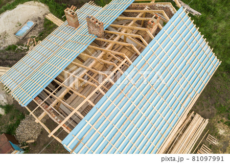 Aerial view of a brick house with wooden roof frame under construction. 81097991