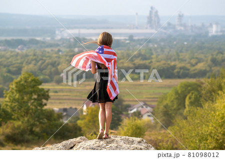 Young happy american woman with long hair holding waving on wind USA national flag on her sholders relaxing outdoors enjoying warm summer day. Young happy american woman with long hair holding waving on wind USA national flag on her sholders relaxing outdoors enjoying warm summer day. 81098012