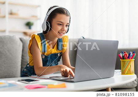 Girl sitting at desk, typing on keyboard, wearing headphones Girl sitting at desk, typing on keyboard, wearing headphones 81098155