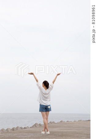防波堤に立つ女性の後ろ姿（手をあげる） 81098961