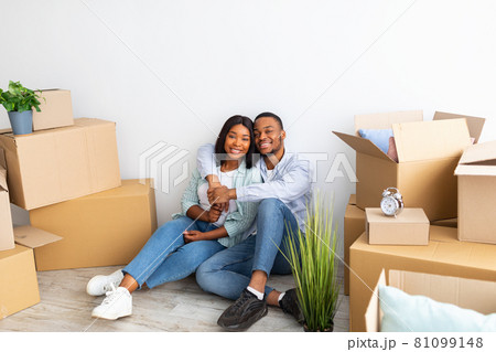 Home relocation concept. Portrait of young black spouses sitting among cardboard boxes after moving to own flat 81099148