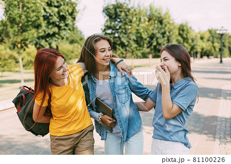 Schoolgirls walk along the park alley to school, talk and laugh. The concept of training and education. Back to school 81100226