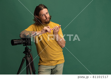 Comic portrait of young man, photographer, cameraman with retro camera having fun isolated on green studio background. Concept of occupation, job, funny meme emotions Comic portrait of young man, photographer, cameraman with retro camera having fun isolated on green studio background. Concept of occupation, job, funny meme emotions 81101517