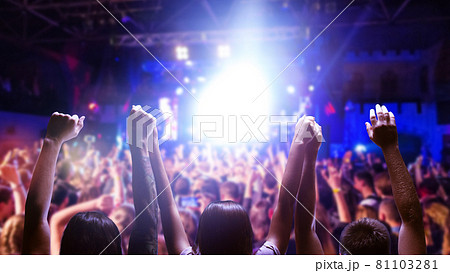 Raised hands of many people in honor of a musical show on stage. People in the hall 81103281