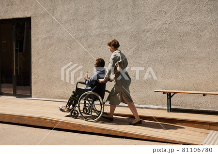 Nurse pushing wheelchair with disabled man 81106780