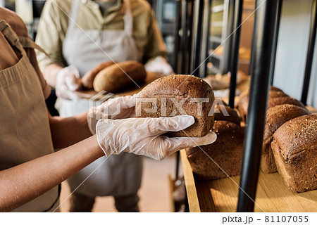 Gloved hands of young woman holding fresh loaf of bread 81107055