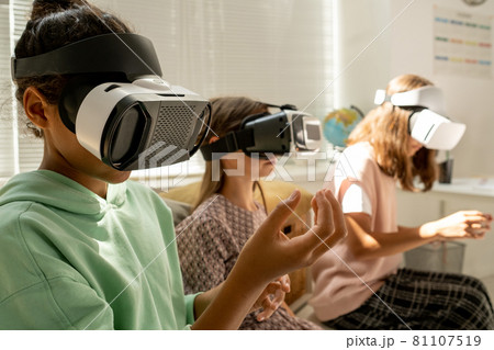 Mixed-race schoolgirl in goggles holding invisible virtual object 81107519