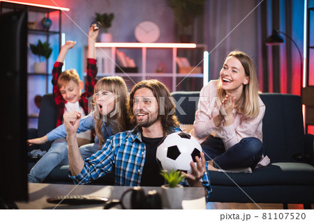 Parents with children enjoying soccer game on TV at home Parents with children enjoying soccer game on TV at home 81107520