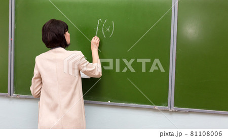 A female teacher writes a mathematical formula on a blackboard 81108006