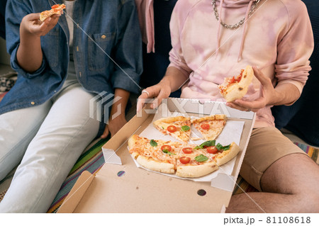 Two teenagers in casualwear eating pizza while sitting on the floor Two teenagers in casualwear eating pizza while sitting on the floor 81108618