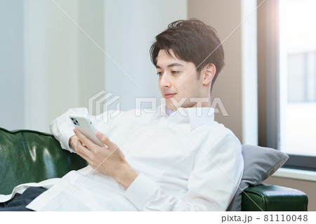 ソファでくつろぎながらスマートフォンを操作する男性 ソファでくつろぎながらスマートフォンを操作する男性 81110048