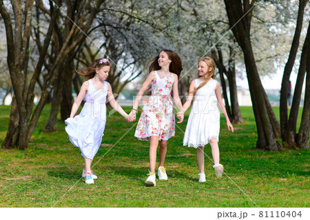 Three adorable girls in dresses hold hands in the garden, park. Three adorable girls in dresses hold hands in the garden, park. 81110404