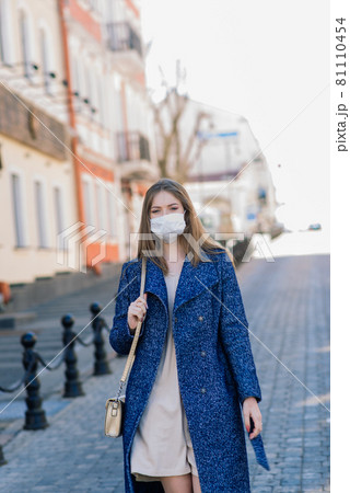 Happy cheerful young woman in face medical mask while standing on street in city. 81110454