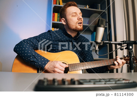 Close-up shoot from below of guitarist singer man play on acoustic guitar recording sing song using professional microphone stand at home studio. 81114300