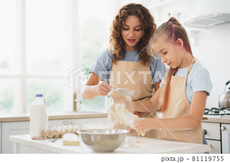 Teen girl helping her mom to cook dough in their kitchen at home 81119755