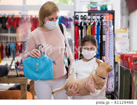 Woman in mask in pet store during shopping with her daughter with dog Woman in mask in pet store during shopping with her daughter with dog 81129466