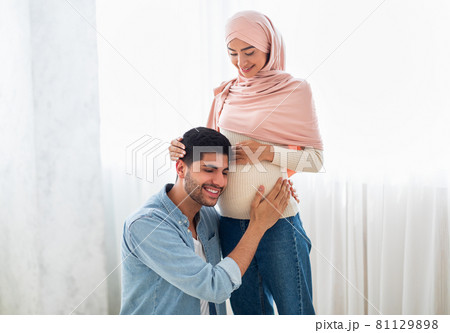 Happy arab man pressing his ear against his wife's pregnant belly, listening to his baby's heartbeat, free space Happy arab man pressing his ear against his wife's pregnant belly, listening to his baby's heartbeat, free space 81129898