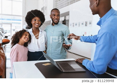 Salesman giving new car key to young Afro family at auto dealership. Vehicle local distribution concept Salesman giving new car key to young Afro family at auto dealership. Vehicle local distribution concept 81129948