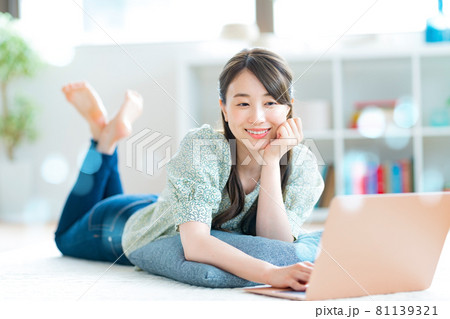 リビングでパソコンを操作するうつ伏せの若い女性の写真素材