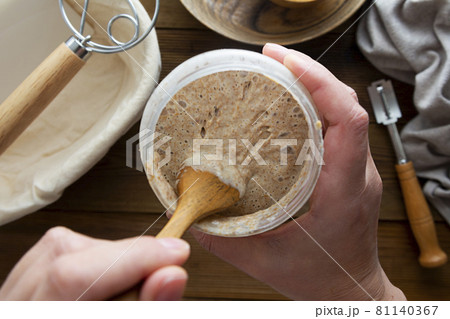 Starter sourdough. Female hands holding a jar with sourdough over wooden background. Starter sourdough. Female hands holding a jar with sourdough over wooden background. 81140367