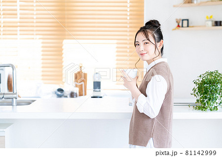 キッチンでコーヒーを飲みながらリラックスする若い女性 81142999