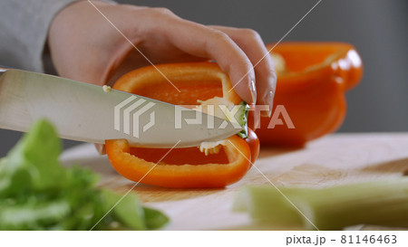 Woman's hands slicing sweet Red Bell Pepper on a wooden cutting board (UHD, 4K) beautiful shot with soft focus. Healthy food concept. 81146463