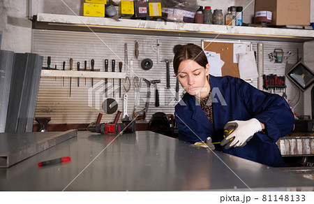 Woman apprentice measures metal sheet with tape measure Woman apprentice measures metal sheet with tape measure 81148133