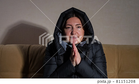Lady in warm jacket with hood tries to heat hands on sofa Lady in warm jacket with hood tries to heat hands on sofa 81151208