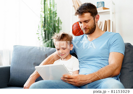 Little boy and his dad watching videos on digital tablet together sitting on sofa Little boy and his dad watching videos on digital tablet together sitting on sofa 81153029
