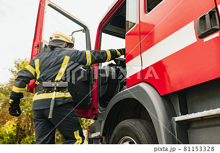 One young male firefighter dressed in uniform with protective helmet climbing into fire truck. One young male firefighter dressed in uniform with protective helmet climbing into fire truck. 81153328