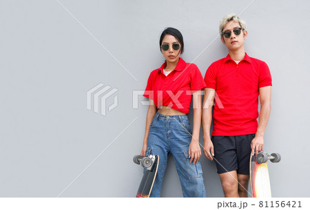 Asian couple resting after skateboarding. Both of them put skateboards leaning against their legs. 81156421