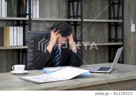 Sad Asian businessman holds his temple with both hands, sitting in the office. The concept of unemployed, sadness, depressed and human problems. 81156525