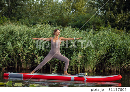 One young Caucasian beautiful slim girl doing yoga, pilates on paddle board, SUP alone in summer morning. Active life, sport, leisure activity concept One young Caucasian beautiful slim girl doing yoga, pilates on paddle board, SUP alone in summer morning. Active life, sport, leisure activity concept 81157805