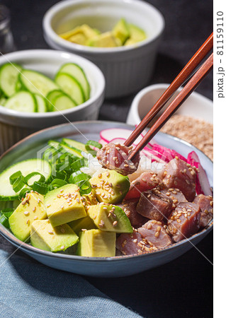 Someone holds piece of tuna fish over Poke Bowl Someone holds piece of tuna fish over Poke Bowl 81159110