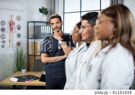 Profile view of diverse team of doctors standing in row with Arab male doctor behind Profile view of diverse team of doctors standing in row with Arab male doctor behind 81161838