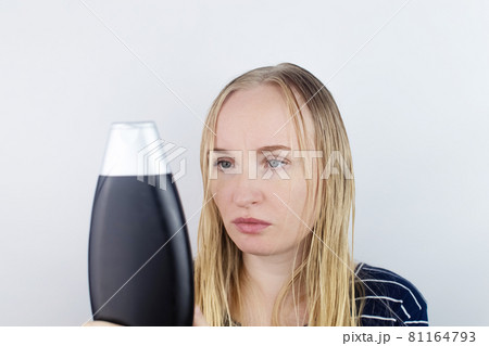 The girl looks in the mirror at her oily hair, then takes a shampoo to treat oily hair. Problematic scalp and increased secretion of the sebaceous glands. Cosmetology diseases treatment concept The girl looks in the mirror at her oily hair, then takes a shampoo to treat oily hair. Problematic scalp and increased secretion of the sebaceous glands. Cosmetology diseases treatment concept 81164793