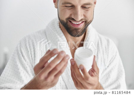 Happy mature man looks at open jar of cream in professional cosmetologycal clinic Happy mature man looks at open jar of cream in professional cosmetologycal clinic 81165484