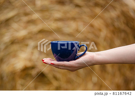 Female hand holds a porcelain cup of coffee on a natural background. Selective focus on the cup. 81167642