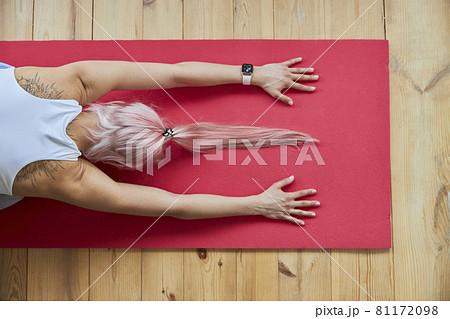 Pink haired lady with smartwatch in white top sits in child pose on floor Pink haired lady with smartwatch in white top sits in child pose on floor 81172098