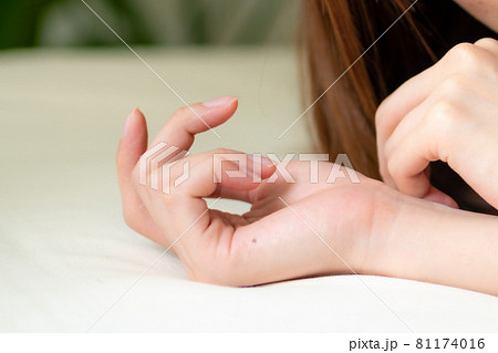 ベッドに横たわる若い女性の手元のイメージ 81174016
