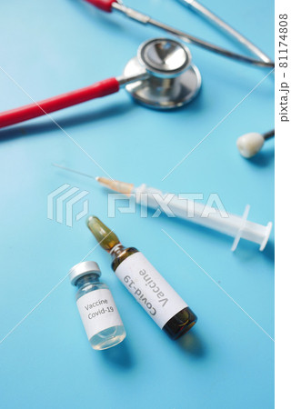 Close up of coronavirus vaccine , stethoscope and syringe on blue Close up of coronavirus vaccine , stethoscope and syringe on blue 81174808