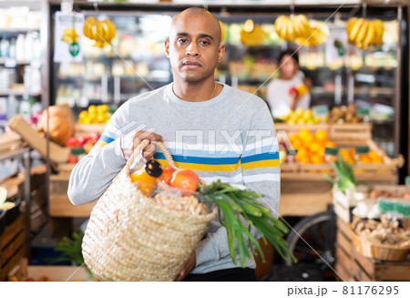 Hispanic man walking with purchases among shelves in supermarket Hispanic man walking with purchases among shelves in supermarket 81176295