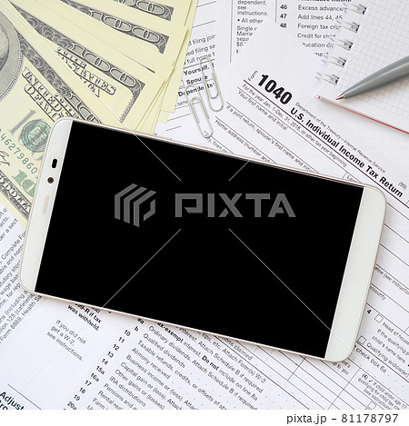 Composition of items lying on the 1040 tax form. Dollar bills, pen, smartphone, paper clip and notepad. Clean black screen smartphone for text placement 81178797
