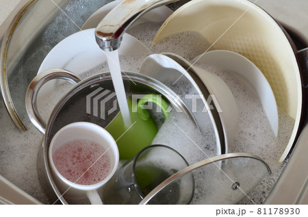 Dirty dishes and unwashed kitchen appliances lie in foam water under a tap from a kitchen faucet 81178930