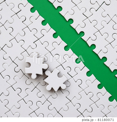 The green path is laid on the platform of a white folded jigsaw puzzle. The missing elements of the puzzle are stacked nearby. Texture image with space for text 81180071