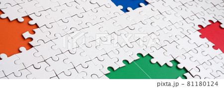 Close-up texture of a white jigsaw puzzle in assembled condition with missing elements, under which surfaces of different colors 81180124