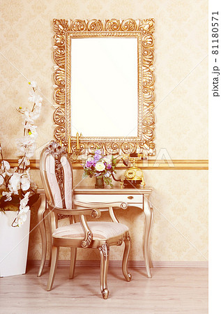 A fragment of a retro interior with a chair and table, on which is a telephone and a vase of flowers. Above the table hangs an empty picture frame for your photo A fragment of a retro interior with a chair and table, on which is a telephone and a vase of flowers. Above the table hangs an empty picture frame for your photo 81180571