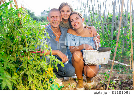 Portrait of daughter and parents with watering cans in summer garden 81181095