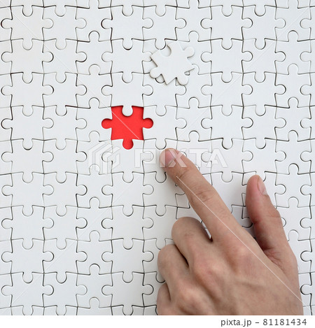 The texture of a white jigsaw puzzle in the assembled state with one missing element, forming a red space, pointed to by the finger of the male hand The texture of a white jigsaw puzzle in the assembled state with one missing element, forming a red space, pointed to by the finger of the male hand 81181434