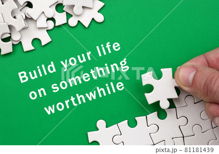 Build your life on something worthwhile. The hand folds a white jigsaw puzzle and a pile of uncombed puzzle pieces lies against the background of the green surface 81181439
